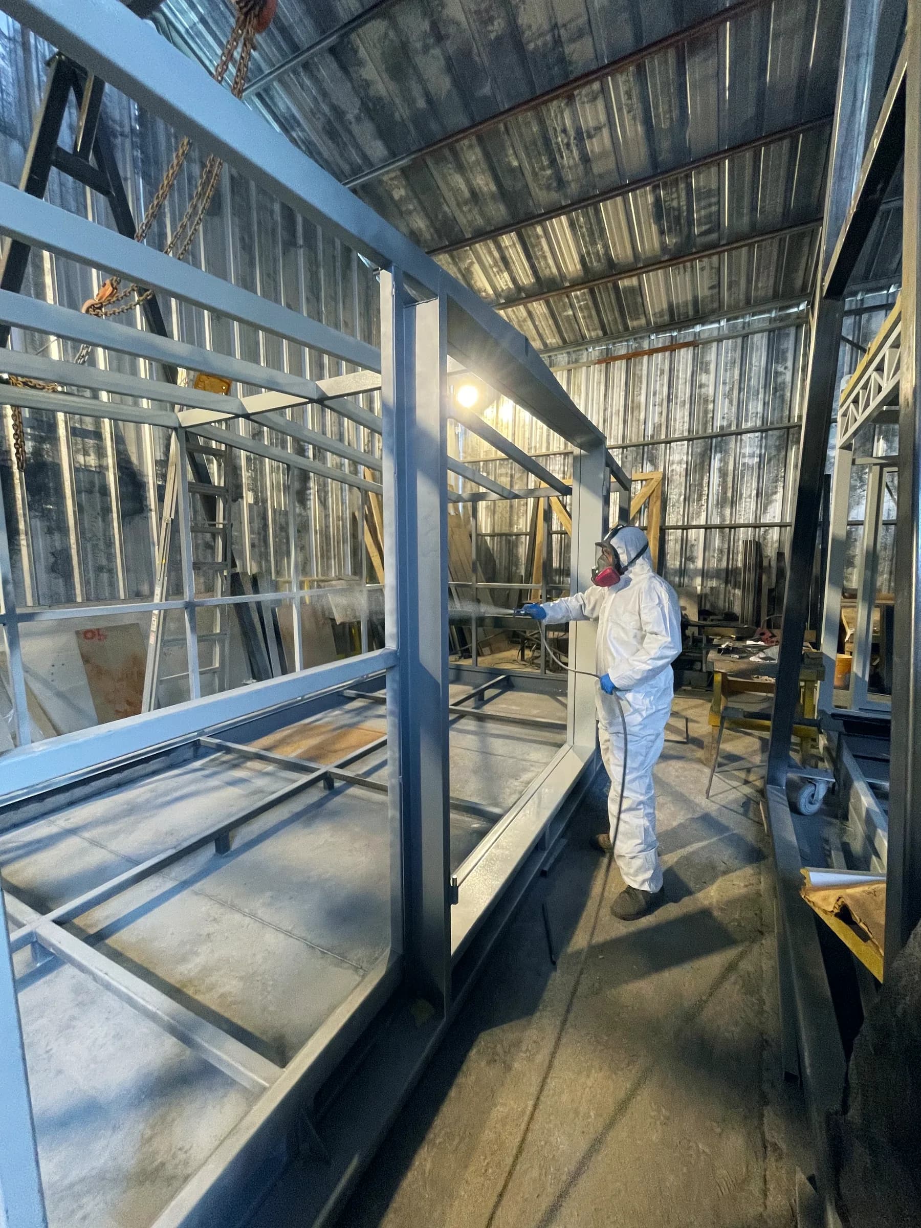 Pintor con traje de protección blanco y respirador aplicando pintura sobre la estructura de un módulo